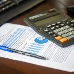 Calculadora, relatório financeiro e caneta sobre uma mesa, representando análise e controle orçamentário.