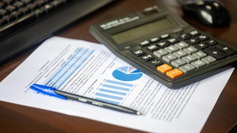 Calculadora, relatório financeiro e caneta sobre uma mesa, representando análise e controle orçamentário.