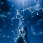 Mão robótica alcança uma rede digital azul, em representação conceitual da inteligência artificial e das tecnologias conectadas.