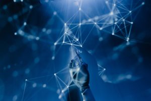 Mão robótica alcança uma rede digital azul, em representação conceitual da inteligência artificial e das tecnologias conectadas.