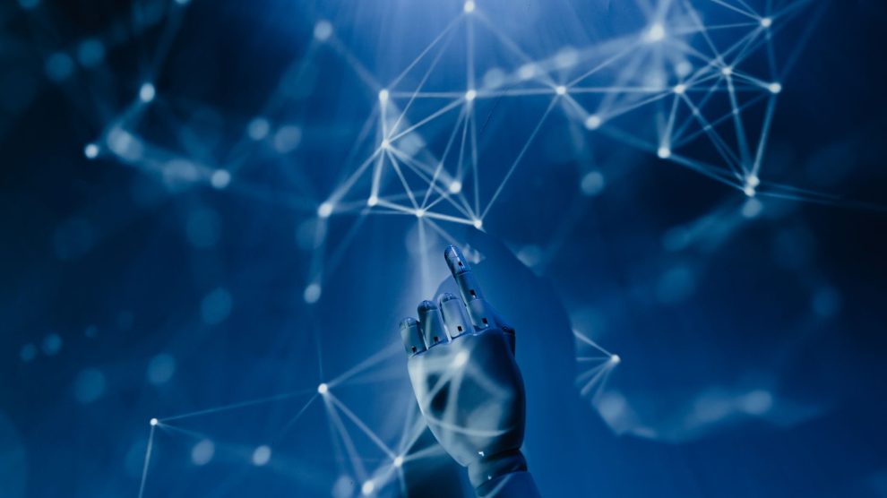 Mão robótica alcança uma rede digital azul, em representação conceitual da inteligência artificial e das tecnologias conectadas.