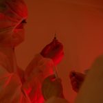 Pesquisadores usando roupas de proteção preparam seringas em um laboratório.