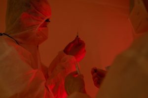 Pesquisadores usando roupas de proteção preparam seringas em um laboratório.