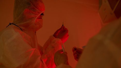 Pesquisadores usando roupas de proteção preparam seringas em um laboratório.