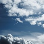 Céu amplo com formações de nuvens e trilhas de condensação deixadas por aviões.