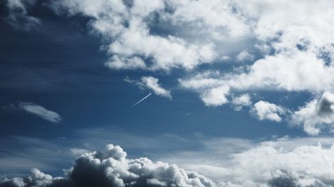 Céu amplo com formações de nuvens e trilhas de condensação deixadas por aviões.