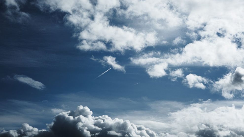 Céu amplo com formações de nuvens e trilhas de condensação deixadas por aviões.