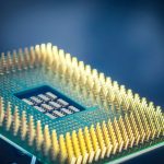 Close-up de um chip de computador com pinos dourados sobre fundo azul.