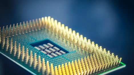 Close-up de um chip de computador com pinos dourados sobre fundo azul.