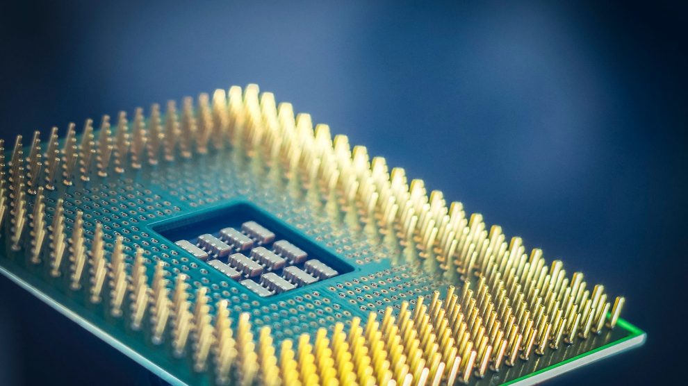 Close-up de um chip de computador com pinos dourados sobre fundo azul.