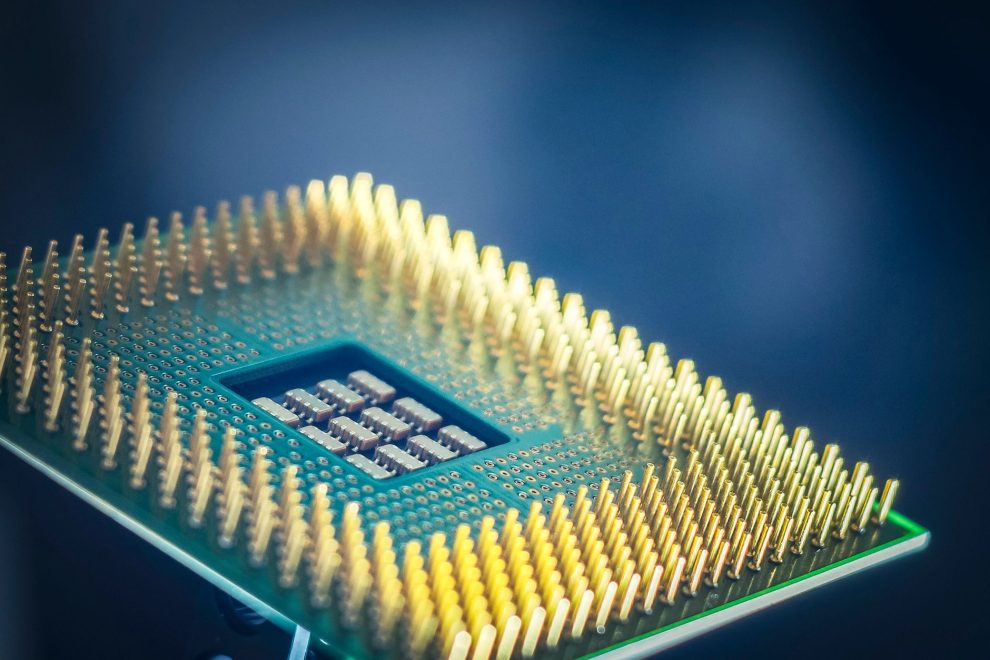 Close-up de um chip de computador com pinos dourados sobre fundo azul.