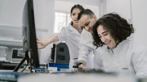 Equipe diversa de cientistas trabalha em conjunto diante de um computador em um laboratório moderno.