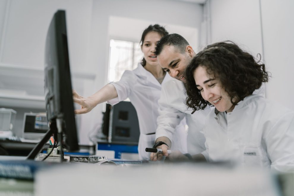 Equipe diversa de cientistas trabalha em conjunto diante de um computador em um laboratório moderno.